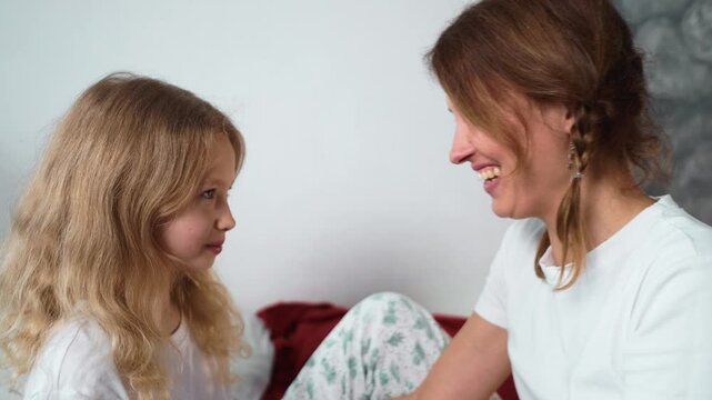 Mom and daughter are relaxing at home, enjoying time together. Girl rubs her nose against her mothers, giggles and shares affection in cozy pajamas. Pure love and joy in every moment. Mothers day