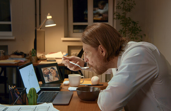 Businessman eating breakfast and working at office desk at night