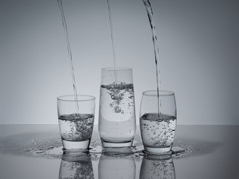 Water streams gracefully fill three glasses, a refreshing scene