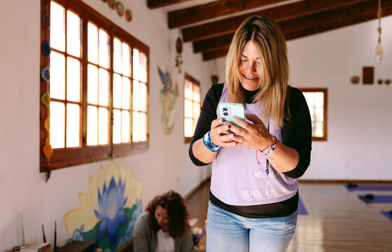 Yoga teacher smiling and using smartphone before meditation class