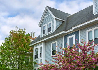 Upper facade of an elegant family house featuring a gable dormer and spring foliage in Brighton, Massachusetts, USA
