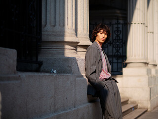 Portrait of handsome Chinese young man wearing gray suit posing in the street, young guy with black curly hair with urban background. Male fashion, cool Asian young man lifestyle.