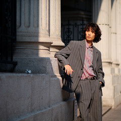 Portrait of handsome Chinese young man wearing gray suit posing in the street, young guy with black curly hair with urban background. Male fashion, cool Asian young man lifestyle.