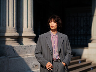 Portrait of handsome Chinese young man wearing gray suit posing in the street, young guy with black curly hair with urban background. Male fashion, cool Asian young man lifestyle.