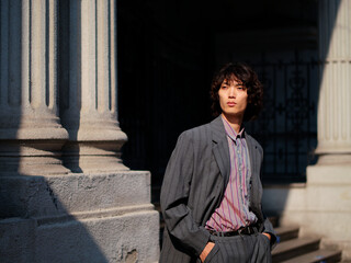 Portrait of handsome Chinese young man wearing gray suit posing in the street, young guy with black curly hair with urban background. Male fashion, cool Asian young man lifestyle.
