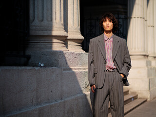 Portrait of handsome Chinese young man wearing gray suit posing in the street, young guy with black curly hair with urban background. Male fashion, cool Asian young man lifestyle.