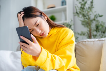 Bad news on device screen. Upset asian woman frustrated by problem with work or relationships, sitting on couch, feeling despair and anxiety, loneliness, having psychological trouble