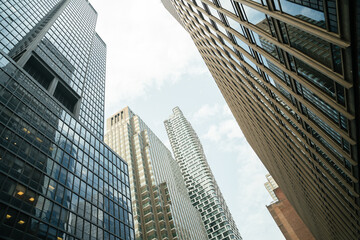 Looking up at a cluster of tall buildings in Midtown Manhattan. Glass reflections and urban geometry dominate the scene.
