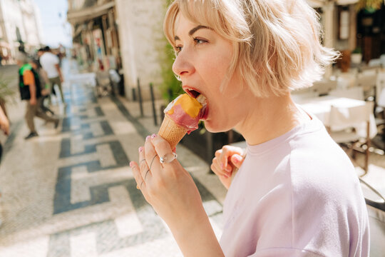 Woman biting colorful ice cream cone during sunny day in Lisbon