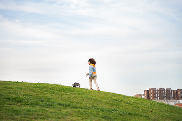 Woman walking a french bulldog in an urban park on a cloudy day