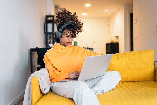 Young woman working from home using laptop and headphones on sofa