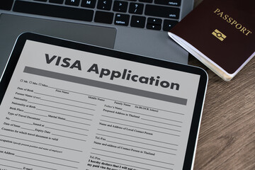 Visa application digital tablet displaying visa application form placed wooden desk with passport and laptop keyboard background, suggesting