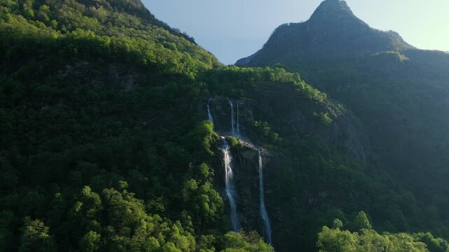 Aerial forward towards spectacular Acquafraggia waterfalls cascading down lush green mountainside in Piuro, Val Bregaglia, Italy, natural wonder. Drone approaching