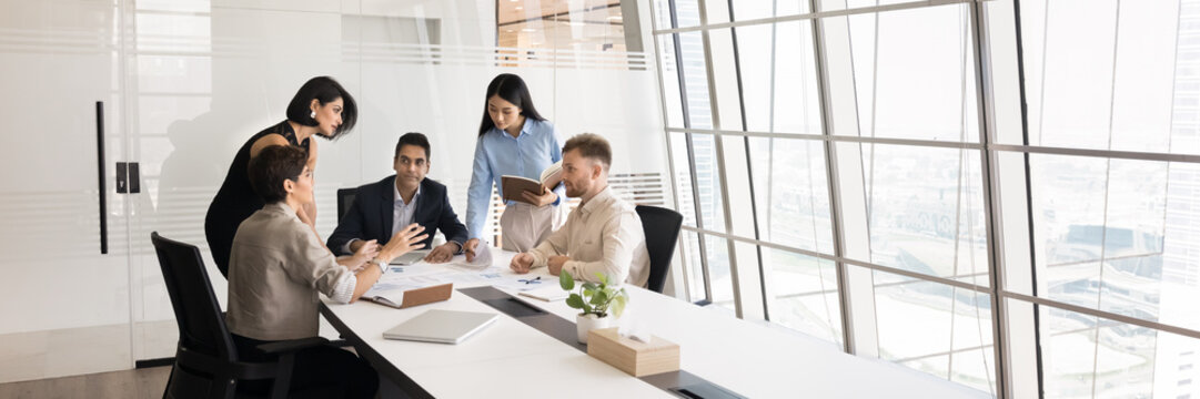 Group of professionals brainstorming gather in modern conference room, panoramic view. Team reviewing documents, exchanging ideas about strategic plan, project updates, or business decisions. Briefing - Powered by Adobe