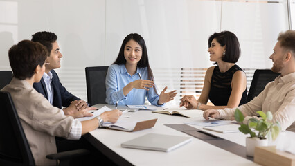 Pretty Asian businesswoman lead business meeting with diverse staff or stakeholders, discussing business-related topic, planning next steps for project, review data, charts, or statistics to analyze