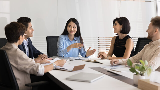 Pretty Asian businesswoman lead business meeting with diverse staff or stakeholders, discussing business-related topic, planning next steps for project, review data, charts, or statistics to analyze