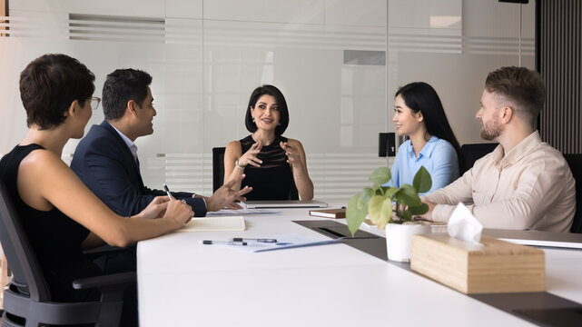 Fototapeta Attractive businesswoman and teammates collaborate on presentation, analyze status of ongoing project, discussing next steps, provide feedback and planning improvements, gathered at conference table
