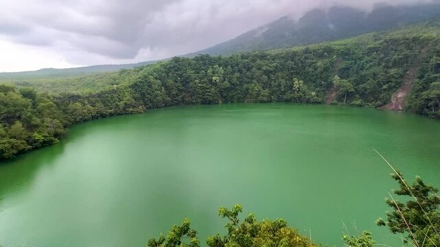 Aerial view of  Lake Tolire in Ternate, Indonesia, with vibrant green water surrounded by lush forest.