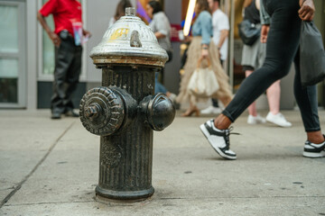 Fire hydrant stands in focus as a crowd walks by on the city sidewalk. Urban moment captured in motion.
