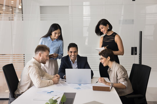 Joyful team gathered around laptop in conference room, engaging in collaborative discussion, enjoy positive and productive teamwork using modern device, review project, learn new AI business software