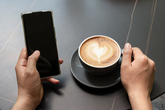 Close-up of a man's hands drinking coffee and looking at his phone in the courtyard - Powered by Adobe