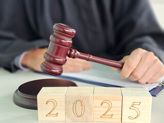 A wooden gavel is raised a judge prepares to make a decision, with numbered blocks showing 2025