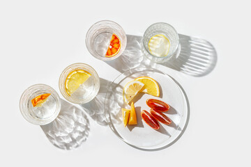 Fruit Infused Water in Glasses and plate with Shadows at sunlight on White background. Aesthetic...