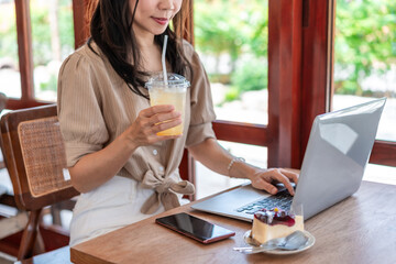 Smiling young Asian woman with drinks working with laptop in cafe, Digital nomad lifestyle