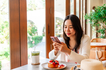 Young woman using smart phone and enjoy eating dessert in cafe on vacation trip
