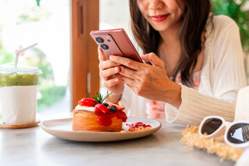 Young woman taking photo of dessert with smart phone for social media in cafe while traveling