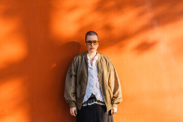 Person standing against orange wall in fashionable outfit