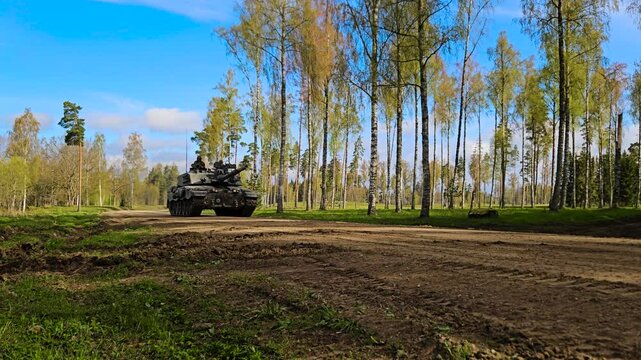 Rare beautiful video footage of a British army Challenger 2 4034 heavy armored tank driving on a dusty countryside gravel forest road during a sunny day with dust coming out from the back.