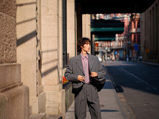 Portrait of handsome Chinese young man wearing gray suit posing in the street, young guy with black curly hair with urban background. Male fashion, cool Asian young man lifestyle.