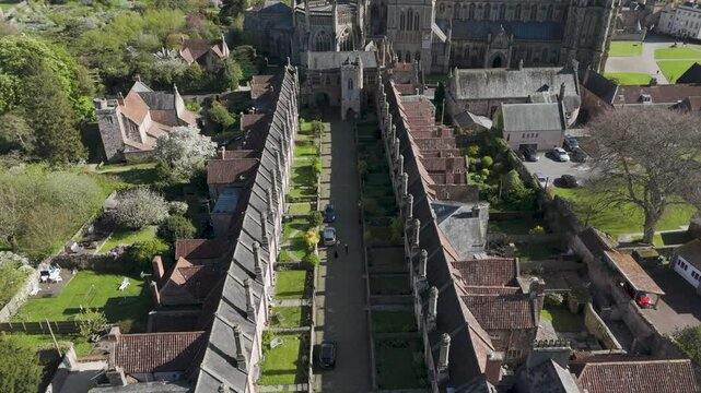 Aerial view of medieval Vicars' Close with parallel stone cottages, tall chimneys and a green central lane converging toward a Gothic cathedral, illustrating preserved heritage living