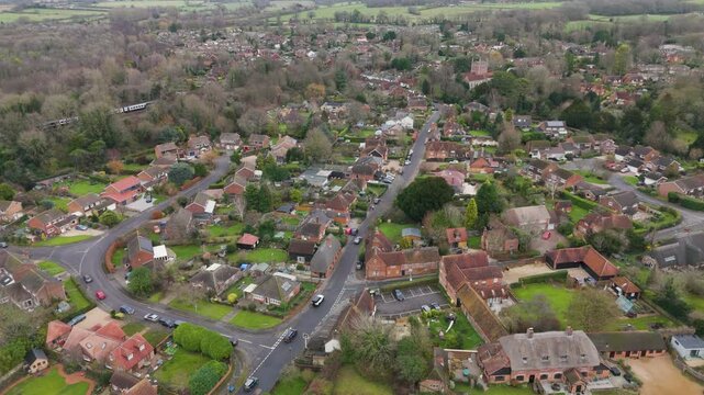 Aerial pan across tree-lined lanes and red-brick homes of rural-suburban village revealing tranquil residential pattern amid open green countryside