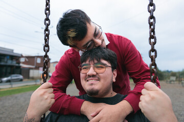 Two men couple having fun on swings in a playground