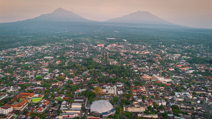 An aerial perspective captures an Indonesian city nestled between two majestic mountains,...