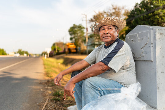 Elderly Thai man resting roadside with collected plastic bottles