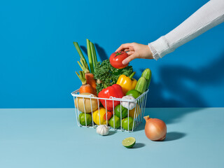 Hand Selecting Fresh Vegetables from a Colorful Basket On Blue Table