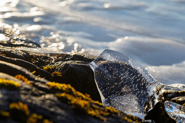 Close-up of a piece of transparent ice on a rock by a frozen lake on a sunny day in the winter. Focus on the foreground.
