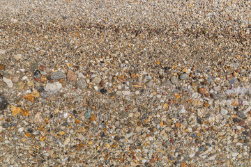 Small pebbles on the shore in a beach and a small wave on sunny day, viewed from above. Abstract natural travel, vacation and summer background.