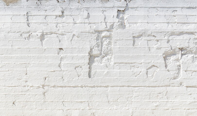 Old, weathered, cracked and plastered concrete wall painted in white on sunny day, viewed from the front. High resolution full frame textured background with copy space.