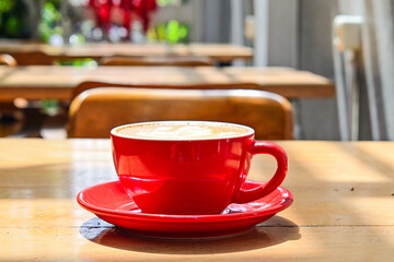 Side view of cafe latte in the red cup. Front, cafe or coffee shop, wooden tables, chairs, copy space, empty, free, text. sun shine, light, bright, dark, shadows, black.