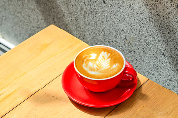 Close up view of hot cafe latte in the red cup. Wooden table, grey or gray wall. Copy space. Coffee. Latte art.
