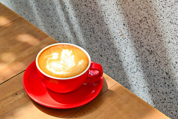 Close up view of hot cafe latte in the red cup. Wooden table, grey or gray wall. Copy space. Coffee. Latte art. Shadows, dark, Black.