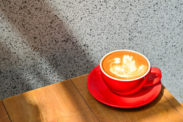 Close up view of hot cafe latte in the red cup. Wooden table, grey or gray wall. Copy space. Coffee. Latte art. Shadows, dark, Black.