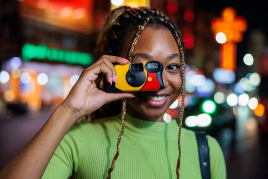 Happy woman photographing through instant camera in city at night