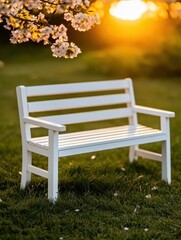 A white bench sits on green grass under blooming cherry blossoms at sunset.
