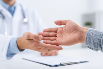 Patient and doctor reaching out to shake hands during medical consultation, showing trust and professional care in clinical setting