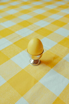 Yellow egg in a silver holder on a checked tablecloth
